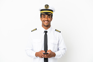 African American Airplane pilot over isolated white background sending a message with the mobile © luismolinero