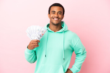 Young man taking a lot of money over isolated pink background posing with arms at hip and smiling