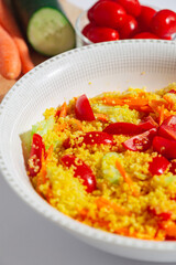 Close up vertical view of cous cous with fresh vegetables, cherry tomatoes, cucumber and carrots over a white background