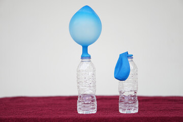 Science experiment , pink inflated balloons and flat balloon on top of transparent test...