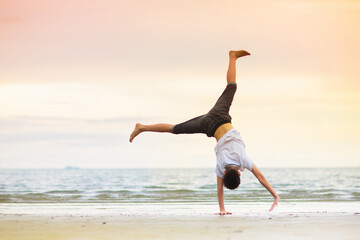 Teenager doing calisthenics exercise. Beach yoga.