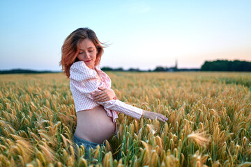 A pregnant woman is holding her stomach in the middle of a wheat field. A girl is expecting a baby at sunset in summer. Fatherhood and motherhood among young people              