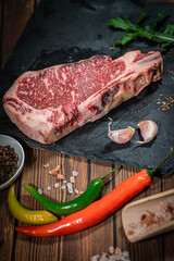 raw cowboy steak with seasonings on wooden background, prime rib eye on bone, top view
