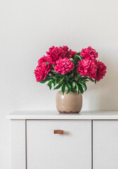 Bouquet of red peonies in a ceramic vase on a white chest of drawers