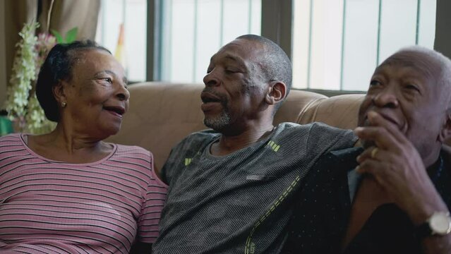 Candid interaction between family members seated on couch. A black  middle-aged son speaking with his elderly parents at home, authentic real life Brazilian people conversing