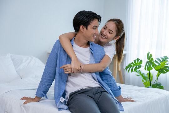 Couple playing in bed at home, hugging soft pillow, nose touching relaxed at home on bed