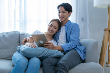 Obraz premium Young couple watching tv series laughing happily using tablet and sitting on sofa bed