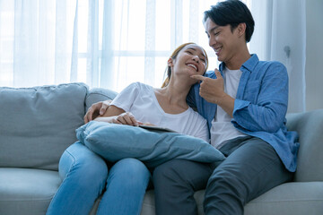 Young couple watching tv series laughing happily using tablet and sitting on sofa bed
