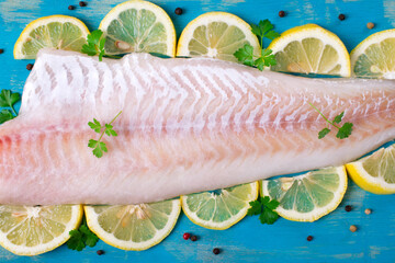 Raw cod fillet on turquoise wooden board with lemon slices, parsley and pepper. Fresh seafood...