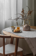 A table set for tea in a cozy living room. A cup of green tea, honey, a sweet bun on a round table
