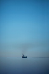 Cargo/ commercial ship traveling in the Aegean Sea in Greece, leaving smoke behind in the sky.
