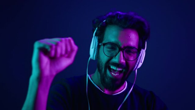 Dancing happy funny excited Indian man crazy moving in headphones dance having fun enjoying song audio sound track Arabian guy dancer listening music movement party in neon club ultraviolet background
