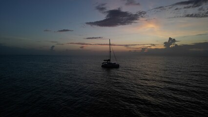 Aerial view of a sailboat anchored off shore as the sun comes up over the ocean