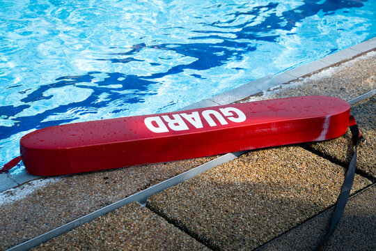 Red guard at swimming pool. Plastic tube lifesaving tool lying beside a pool. 