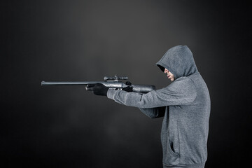 Hooded man with rifle over dark misty background