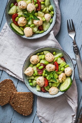 Summer salad with cucumber, mini tomatos, mini mozzarella and soybeans on light blue wooden background