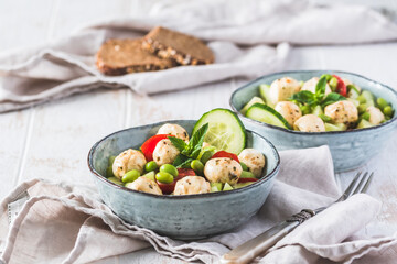 Summer salad with cucumber, mini tomatos, mini mozzarella and soybeans on white wooden background