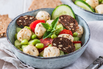 Summer salad with cucumber, mini tomatos, mini mozzarella and soybeans on white wooden background