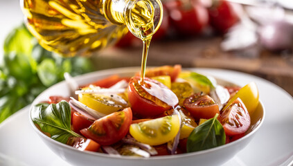 Olive oil is pouring on fresh tomato salad mixed with red onion