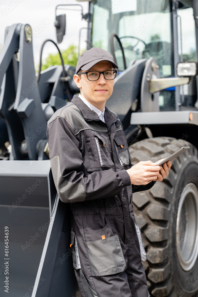 Poster serviceman with digital tablet on a background of the tractor.
