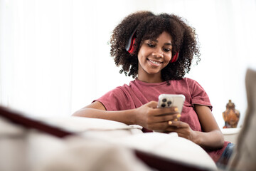 African American woman using the smartphone and listening musics on the sofa - obrazy, fototapety, plakaty