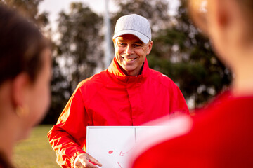 Football coach explaining strategy to his team of tween girls