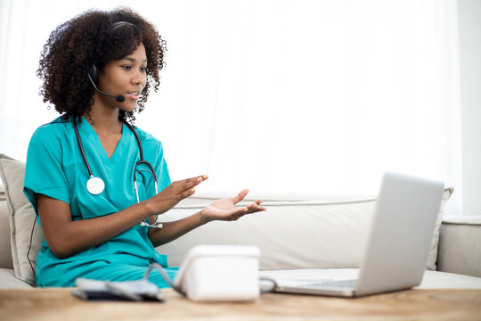 Shot Of Africa American Female Doctor Talking With Colleagues Through A Video Call With A Laptop In The Consultation. Teleconference And Home Health Care Concept.