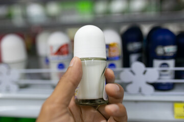 Hand holding deodorant bottle on shelf in supermarket blur background.