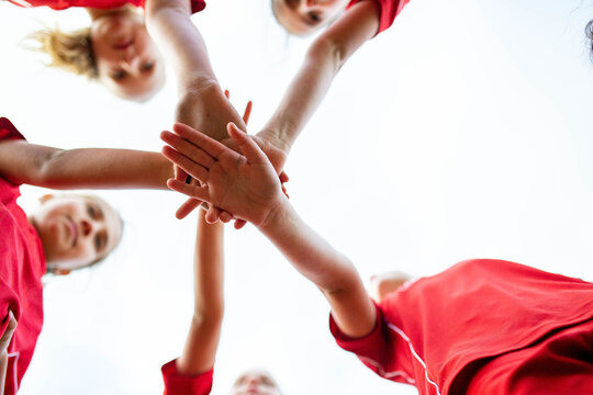 An upward view of tween girls football team joining hands