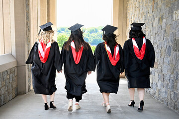 Lifestyle portrait from back of group of female college graduates holding hands walking in a row...
