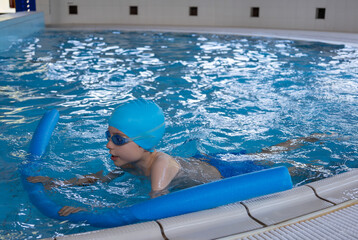 Close up boy swimmer o school boy learning how to swim in a pool wearing in swimming cap and goggles