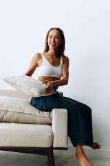 A woman with long hair plays with a pillow sitting on the couch at home and smiles