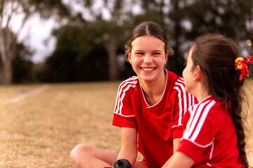 Female football players sitting on the grass taking a break and talking