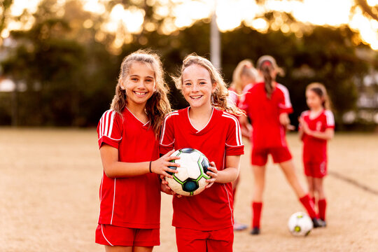 Two tween football players standing together at a sports oval holding a soccer ball
