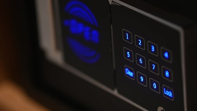 Man hand with a metal strongbox door close up. Unknown person entering numbers combination on electronic panel to lock modern safe. Male fingers pressing locker buttons using correct passcode.