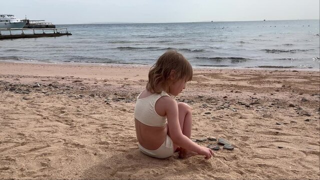 Little cute girl by the sea. Child playing in the sand on the beach