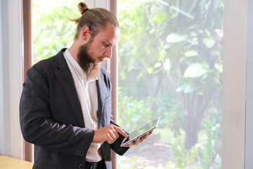 Bearded young businessman holding and working on tablet