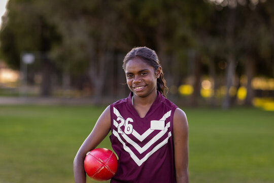 female aboriginal school student holding football under arm
