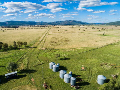Pathway towards hills on flat grassy farm with silos and green paddocks