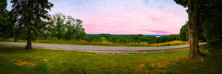 Panoramic sunset over Hudson Valley's hilly meadow and forest with a paved road in upstate New York