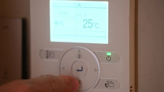 Closeup the man hand controls and presses the buttons The air conditioning and heating control panel for the apartment and office is located on a white wall. Close up