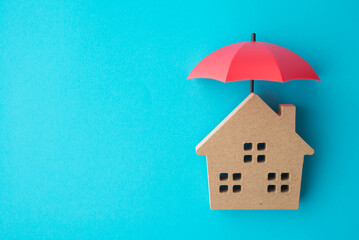 Red umbrella cover home model on blue background copy space. House, real estate, property insurance...