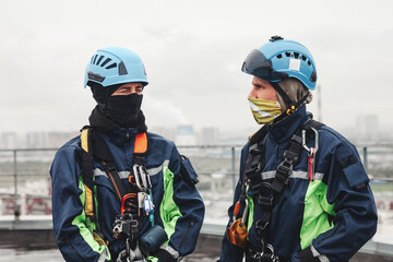 Two industry mountaineer laborers in uniform and helmets posing on roof, looks at each other....