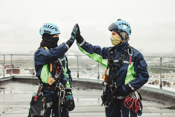 Two industry mountaineer laborers in uniform and helmets posing on roof high rise work. Access...