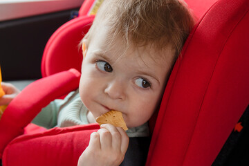 Portrait of  toddler girl sitting in car seat and eating cookies. Child transportation safety