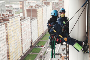 Industry mountaineer laborers hangs over residential house facade. Two workers in uniform and helmets working on wall building, access high rise work. Industrial urban work concept. Copy ad text space