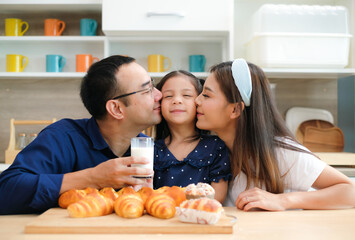 Cute little girl happily in the kitchen as her father and mother lovingly kiss her daughter on the...