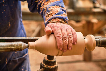 older artisan turner touching with his hand the cylindrical piece of wood he is turning - obrazy, fototapety, plakaty