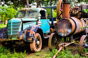 Carcass of a truck and a very old tractor. Old and vintage model of metal tractor and truck. Vintage truck and tractor made of metal on a farm. Very old truck and tractor rusty due to age.