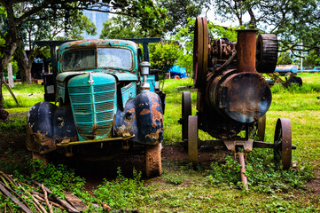 Carcass of a truck and a very old tractor. Old and vintage model of metal tractor and truck. Vintage truck and tractor made of metal on a farm. Very old truck and tractor rusty due to age.